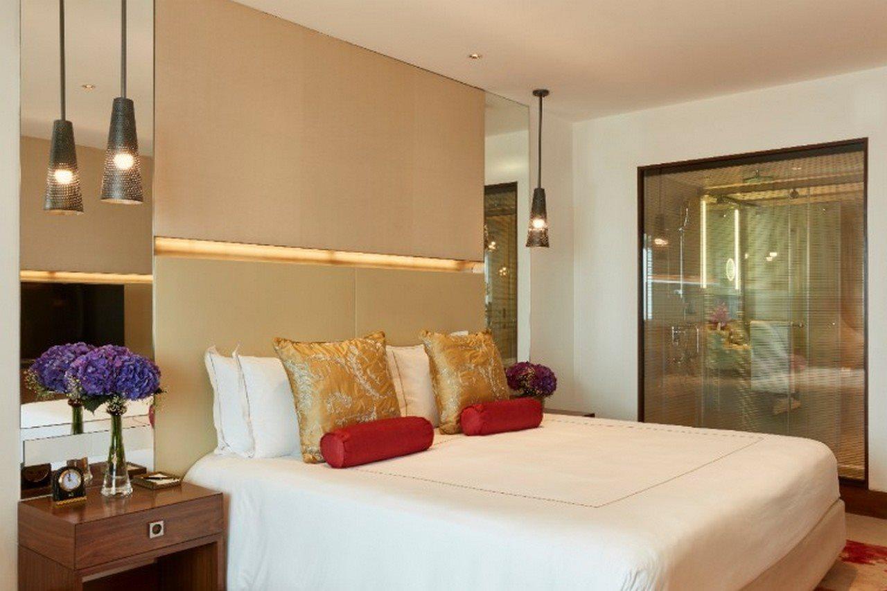 The Taj Mahal Tower, Mumbai Hotel Kültér fotó The photo shows a modern bedroom with a stylish design. It features a large bed with white linens and decorative pillows in gold and red. The walls are neutral, and there are pendant lights hanging above the bed. To the side, there is a wooden nights