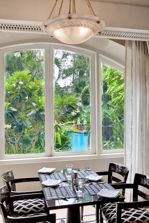 The Taj Mahal Tower, Mumbai Hotel Kültér fotó The photo shows a bright, airy indoor space with large windows framing a lush, green outdoor scene. Through the windows, you can see vibrant foliage, including various tropical plants and trees, creating a natural backdrop. In the distance, there is 
