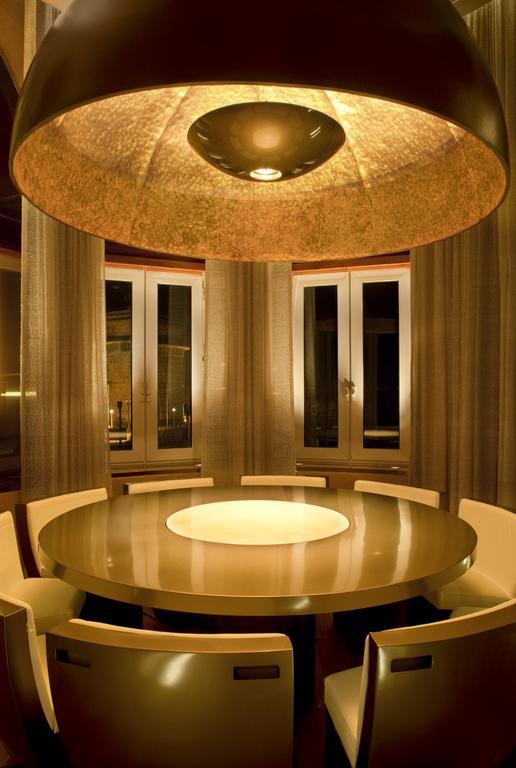 The Taj Mahal Tower, Mumbai Hotel Kültér fotó The photo shows a modern dining room with a round table at the center. The table has a glossy surface and features a circular illuminated section in the middle. Surrounding the table are sleek, contemporary chairs. The room has large windows dressed 