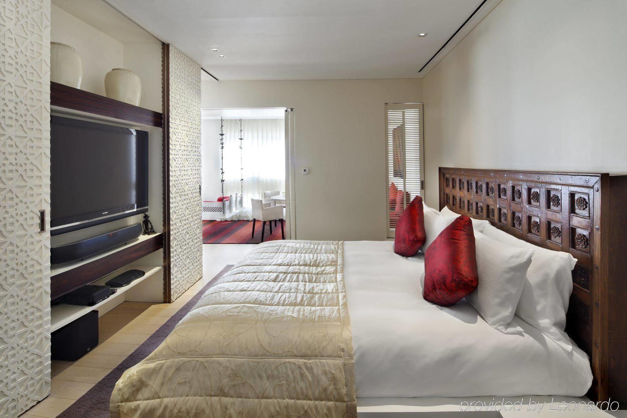 The Taj Mahal Tower, Mumbai Hotel Kültér fotó The photo depicts a modern hotel bedroom. The room features a large bed with white bedding and decorative red pillows. A beautifully carved wooden headboard adds an elegant touch. In the background, there is a flat-screen TV mounted on the wall, alon