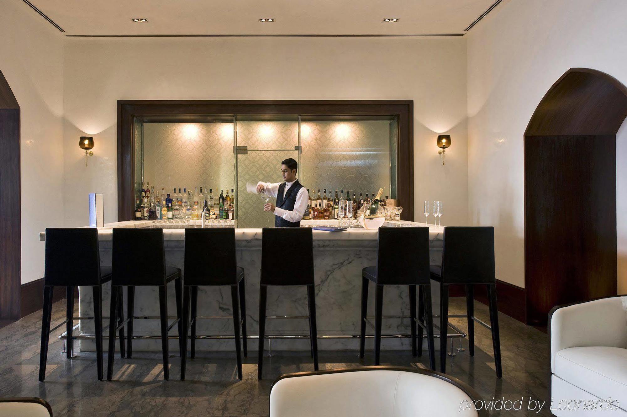 The Taj Mahal Tower, Mumbai Hotel Étterem fotó The photo shows a stylish bar area. In the center, a bartender, dressed in a formal outfit, is standing behind a sleek, modern bar counter made of marble. The bar is lined with high chairs for patrons. Behind the bartender, there are shelves filled w