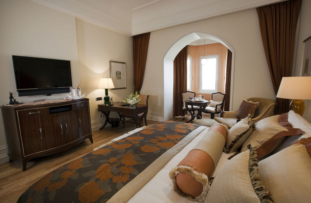 The Taj Mahal Tower, Mumbai Hotel Kültér fotó The photo shows a beautifully arranged hotel room featuring a king-size bed with decorative pillows and a stylish bedspread. Beside the bed is a modern wooden dresser with a flat-screen TV mounted on the wall. There is a cozy seating area with two ch