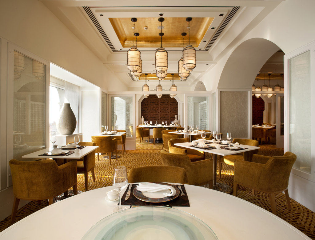 The Taj Mahal Tower, Mumbai Hotel Kültér fotó The photo shows an elegantly designed restaurant interior. The space features stylish furnishings, including round tables topped with white tablecloths and plush, mustard-colored chairs. The ceiling has a decorative design, with pendant lights hangin